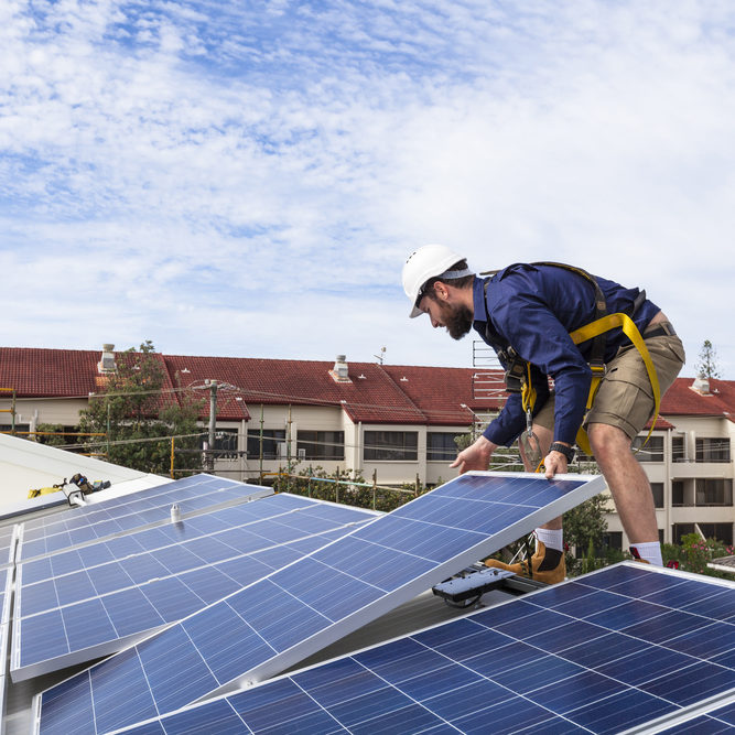 Solar panel technician installing solar panels on roof